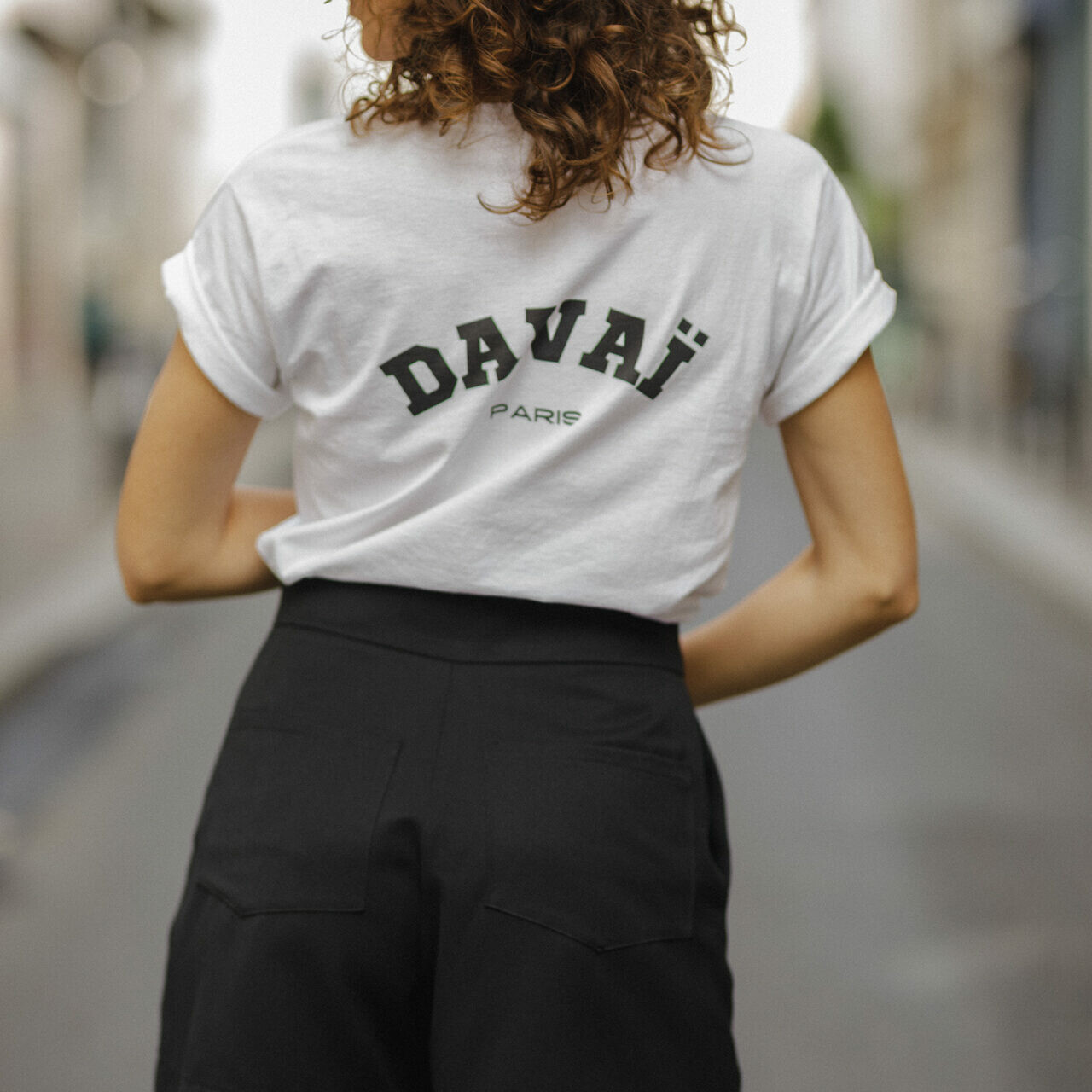 femme portant le t-shirt blanc Davaï et la jupe short noir, vue de dos dans les rues de Paris