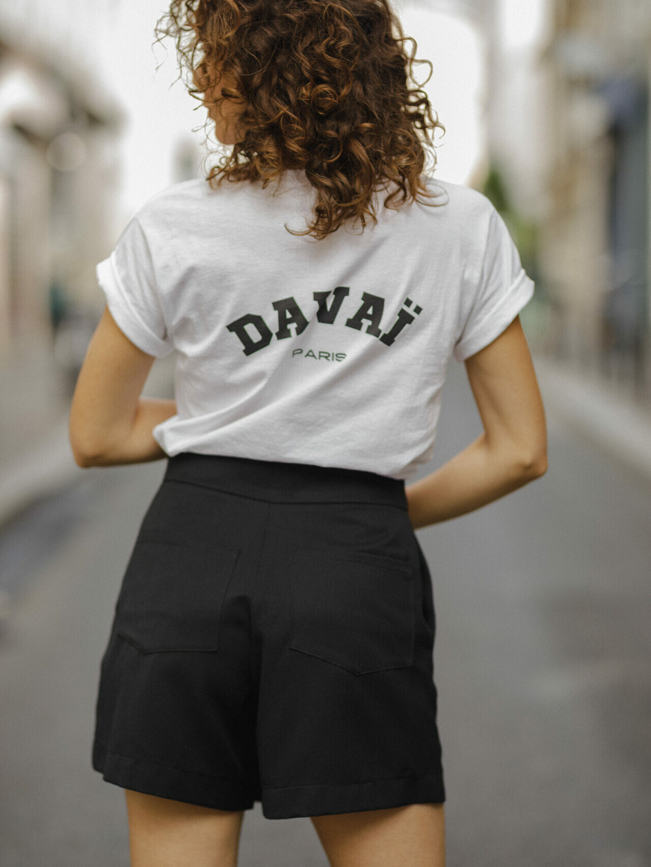 femme portant le t-shirt blanc Davaï et la jupe short noir, vue de dos dans les rues de Paris
