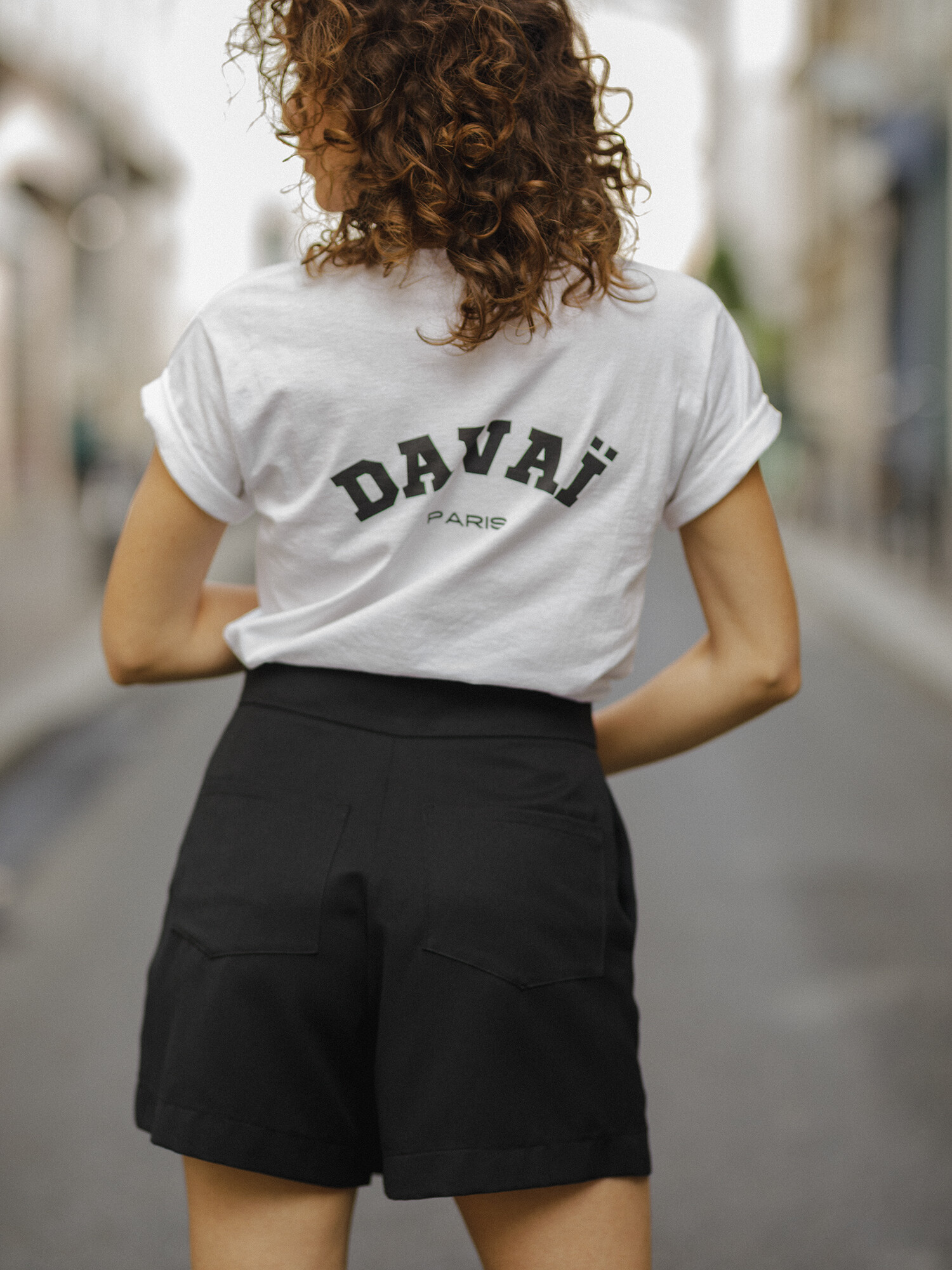 femme portant le t-shirt blanc Davaï et la jupe short noir, vue de dos dans les rues de Paris